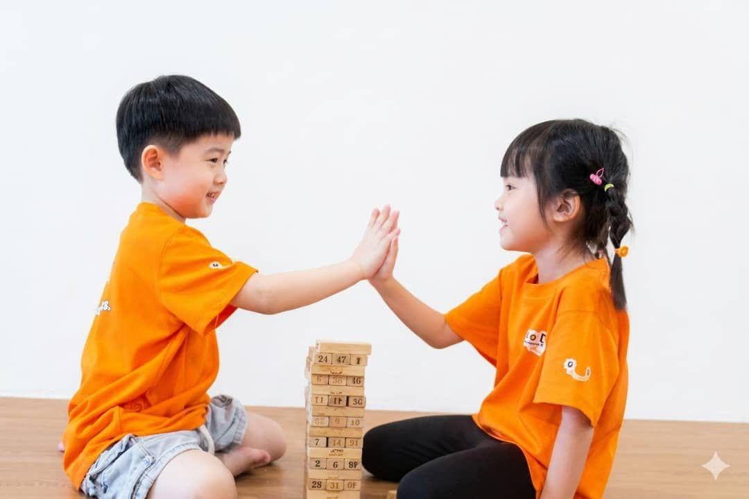 Two DuoDuo children high-five over a block tower